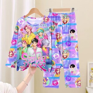 May include: A two-piece pajama set featuring a long-sleeved top and pants. The set is predominantly purple with a repeating pattern of anime-style characters and stars. The top has a large graphic of a group of anime characters and the text "Sale Jump".