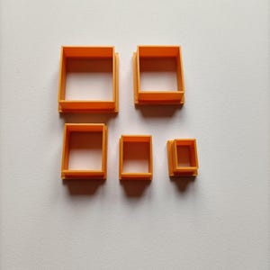 Op de afbeelding: Vijf oranje vierkante koekjessnijders van verschillende maten zijn gerangschikt op een wit oppervlak. De snijders zijn gemaakt van een solide, ondoorzichtig materiaal en hebben een uniforme kleur. De maten variëren en bieden een set gereedschappen voor bakken of knutselen.