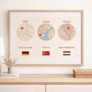 May include: A framed print displaying circular map illustrations of Berlin, Istanbul, and Budapest, each with a heart icon. Below each map are the flags of Germany, Turkey, and Hungary. The print is displayed on a light-coloured wall.