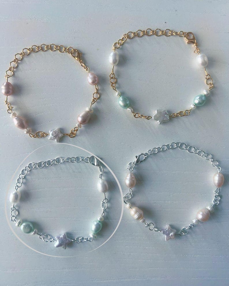 Op de afbeelding: Vier armbanden met zoetwaterparels en sterbedels. Twee armbanden hebben goudkleurige schakels en de andere twee hebben zilverkleurige schakels. De parels zijn wit, roze en lichtgroen.
