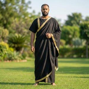 May include: A black floor-length tunic featuring short sleeves and a round neckline, accented with a metallic gold trim along the edges. The garment drapes across the torso and falls to the ankles, creating a structured silhouette with gold detailing.