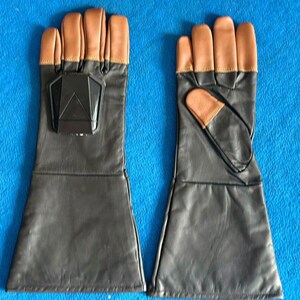 Pode incluir: Um par de luvas de couro preto com pontas dos dedos castanhas e um detalhe geom&eacute;trico preto nas costas de uma luva. As luvas t&ecirc;m um design de punho longo.