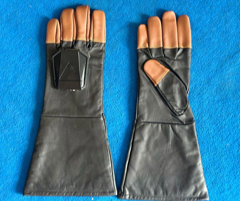 Pode incluir: Um par de luvas de couro preto com pontas dos dedos castanhas e um detalhe geom&eacute;trico preto nas costas de uma luva. As luvas t&ecirc;m um design de punho longo.