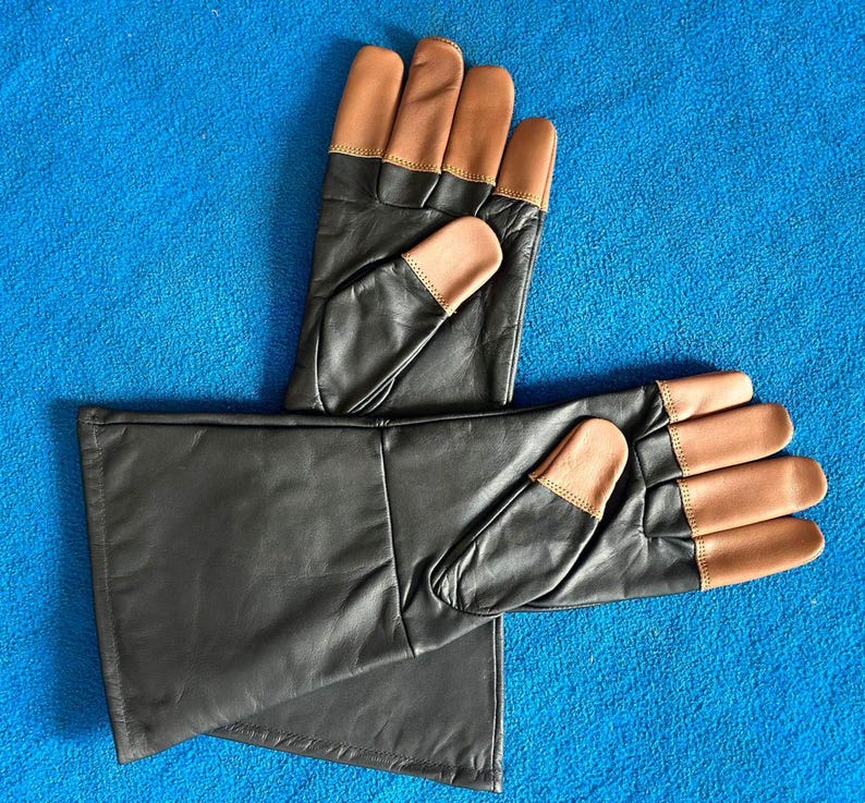 Pode incluir: Um par de luvas de couro preto com pontas e detalhes em castanho. As luvas est&atilde;o sobre uma superf&iacute;cie azul. As luvas parecem novas.