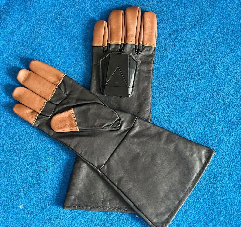 Pode incluir: Um par de luvas de couro preto com pontas dos dedos e detalhes na palma da m&atilde;o em castanho claro. Cada luva tem um design geom&eacute;trico preto nas costas da m&atilde;o. As luvas s&atilde;o exibidas em uma superf&iacute;cie azul.