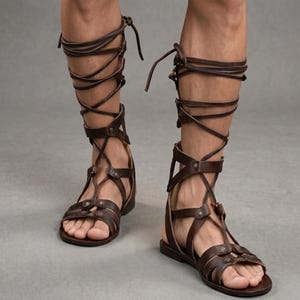 Puede incluir: Sandalias gladiadoras de cuero marrón con múltiples correas y un diseño con cordones. Las sandalias se extienden hasta la pantorrilla y tienen una suela plana. El calzado está diseñado con una serie de correas y hebillas para un ajuste seguro.