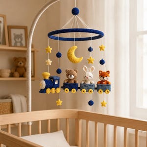 May include: A crochet baby mobile featuring a dark blue circular frame suspended from a curved arm. Hanging elements include a yellow crescent moon, yellow stars, dark blue spheres, and a train with a bear, a white rabbit, and a fox in cars.