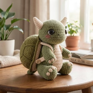 Op de afbeelding: Een handgemaakte gehaakte schildpoppenpop in groen- en beigetinten. De schildpad heeft grote zwarte ogen, kleine hoorns en een schild met een geometrisch patroon. Het zit op een houten tafel, met planten en boeken op de achtergrond.