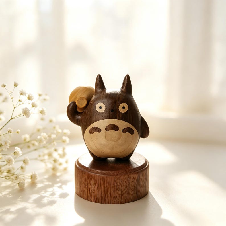 May include: A wooden figurine of a cartoon character with a dark brown body and light brown accents. The figure is standing on a round, wooden base. The character has large eyes and a friendly expression. It is holding a small, round object.