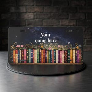 May include: A rectangular license plate featuring a row of colorful, patterned book spines topped with a field of small flowers against a dark, starry night sky background. The text "Your name here" is printed in white in the center of the plate.