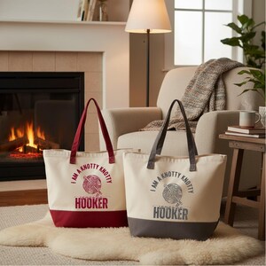 May include: Two canvas tote bags with flat bottoms and dual handles. The left bag is cream with a dark red base and red text reading I AM A KNOTTY KNOTTY HOOKER. The right bag is cream with a dark gray base and gray text reading I AM A KNOTTY KNOTTY HOOKER.