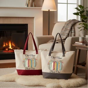 Two tote bags with a book club design are placed on a rug in front of a fireplace, with a lamp and a plant nearby.