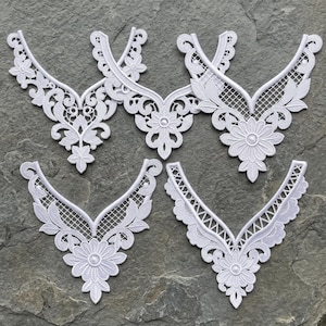 May include: Five white lace collar appliques arranged in a group. Each piece features a V-shaped neckline design with intricate floral embroidery, scalloped edges, and a delicate grid-like mesh pattern throughout the white fabric construction.