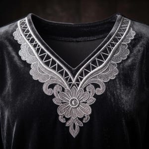 May include: A black velvet top featuring a V-neckline adorned with intricate silver embroidery. The embroidery includes a central floral motif at the base of the neck, surrounded by scalloped edges and geometric lattice patterns along the collar.