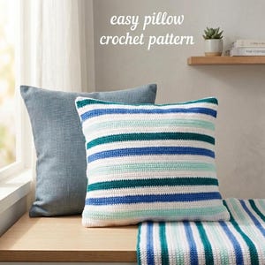 May include: Two decorative cushions, one plain blue and one with horizontal stripes in white, teal, and blue. The text "easy pillow crochet pattern" is visible in the upper centre. The cushions are on a wooden surface.