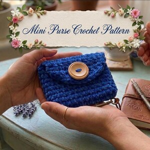 May include: A handmade blue crochet mini purse with a large wooden button closure. The purse is held in two hands. The image also includes a sign that says "Mini Purse Crochet Pattern".