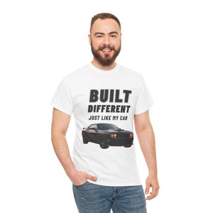 Könnte beinhalten: Weißes T-Shirt mit dem Text "BUILT DIFFERENT JUST LIKE MY CAR" in Schwarz. Unter dem Text ist ein schwarzes Auto abgebildet. Das T-Shirt besteht aus einem weichen Material.