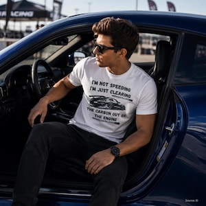 Könnte beinhalten: Ein weißes kurzärmeliges T-Shirt mit einer schwarzen Grafik eines Sportwagens und dem Text: I'M NOT SPEEDING I'M JUST CLEARING THE CARBON OUT OF THE ENGINE. Das T-Shirt wird mit einer dunklen Hose von einer Person mit dunklem Haar getragen.
