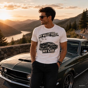 Könnte beinhalten: Ein weißes Kurzarm-T-Shirt mit einer schwarzen Grafik eines klassischen Muscle-Cars, schwebenden Geldscheinen und dem Text "MY WALLET HATES MY CAR", der in einer fetten, abgenutzten Schrift auf der Brust gedruckt ist.
