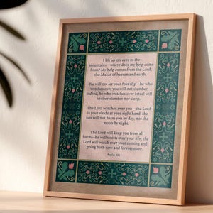 Può includere: Una stampa artistica incorniciata con il testo del Salmo 121 in nero su sfondo rosa chiaro. Il bordo presenta un motivo decorativo verde acqua scuro con foglie verdi, fiori rosa e piccole croci. La cornice è realizzata in legno chiaro.
