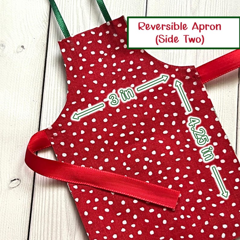 May include: A red and white polka dot reversible apron with green and red ribbon ties. The apron measures 7.6 cm by 10.8 cm. The text "Reversible Apron (Side Two)" is in a green and white box.