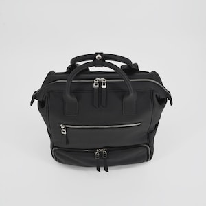 Pode incluir: Uma mochila preta com acabamento texturizado, apresentando uma alça superior com fecho de botão de pressão, um compartimento principal com zíper e dois bolsos horizontais adicionais com zíper na frente. Inclui puxadores de zíper em metal prateado.