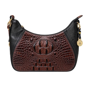 Puede incluir: Un bolso de estilo hobo con un panel central marrón con relieve de cocodrilo, contrastado por paneles laterales negros texturizados. El bolso incluye un cierre de cremallera superior, herrajes dorados y un dije circular dorado con la inscripción Brahmin Est. 1982.
