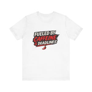 Könnte beinhalten: Weißes T-Shirt mit dem Text "FUELED BY CAFFEINE & DEADLINES" in Schwarz und Rot. Eine kleine rote Chili-Pfeffer-Grafik befindet sich unter dem Text. Das T-Shirt hat einen Rundhalsausschnitt und kurze Ärmel.