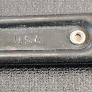 May include: Black adjustable wrench with a circular opening on one end and a hole on the other. The text "MADE IN U.S.A." is visible on the tool. The wrench is made of metal and has a matte finish.