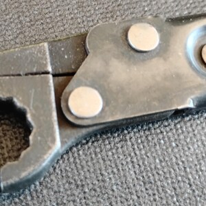 May include: A black metal ratcheting wrench head featuring a twelve-point socket opening. The tool includes a pivoting mechanism secured by two silver-colored circular rivets, with a textured matte finish on the main body of the wrench.
