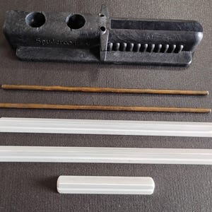 May include: A black tool with two holes and the text "Spudco" is displayed. Two bronze rods and three white, rectangular pieces are also shown. The items are arranged on a dark surface.
