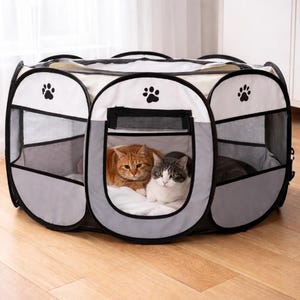 May include: A portable pet playpen in grey, white, and black. The playpen has mesh windows and paw print details. Two cats, one ginger and one grey and white, are inside the playpen.