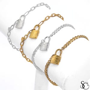 May include: Four bracelets in silver and gold tones, each featuring a padlock charm engraved with the word "love". The bracelets have different chain styles, including a link chain and a curb chain. The bracelets are displayed on a white surface.