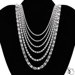 May include: A collection of silver necklaces displayed on a black mannequin. The necklaces vary in length and chain style, creating a layered effect. The chains have a shiny, reflective surface, and the background is a solid black.
