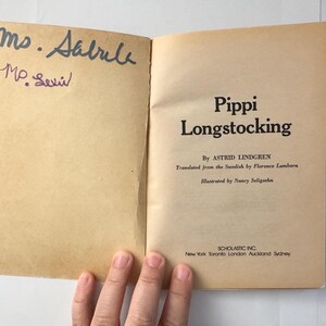 Puede incluir: Un libro abierto con el t&iacute;tulo "Pippi Longstocking" de Astrid Lindgren. Las p&aacute;ginas est&aacute;n envejecidas y tienen notas manuscritas. La portada muestra el logotipo de Scholastic Inc. y los lugares de publicaci&oacute;n.