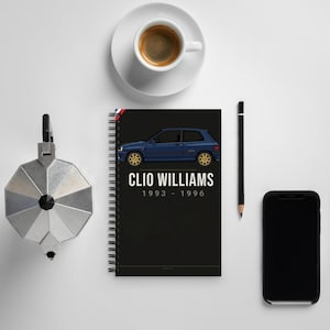 May include: A black spiral-bound notebook featuring a blue car illustration with gold wheels. The text "CLIO WILLIAMS 1993 - 1996" is printed below the car. A cup of coffee, a pencil, a phone, and a silver coffee maker are also visible.