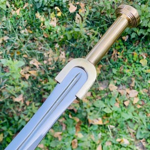 Könnte beinhalten: Ein Schwert mit einer polierten, silberfarbenen Stahlklinge und einem goldfarbenen Messinggriff. Der Griff besteht aus einem zylindrischen Schaft, einem runden Knauf mit konzentrischen Ringen und einem U-förmigen Parier, das mit der Klinge verbunden ist. Der Text Legends Of Handi Crafts ist auf dem Bild zu sehen.