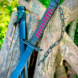 May include: A black sword with a matching scabbard, featuring a handle wrapped in black cord over a bright red underlay. A black metal chain is attached to the pommel, ending in a small U-shaped metal piece. The blade is straight and dark.
