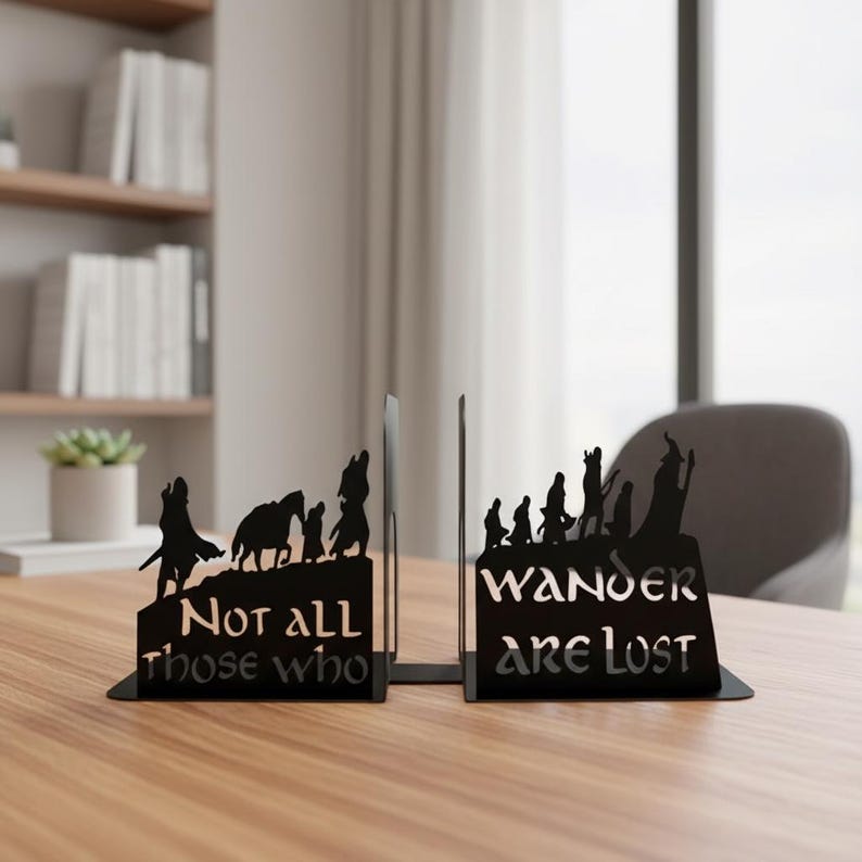 May include: Black metal bookends with a silhouette design. One bookend reads "Not all those who" and the other reads "Wander are lost". The bookends feature a mountain scene with figures and animals. Decorative and functional for any bookshelf.
