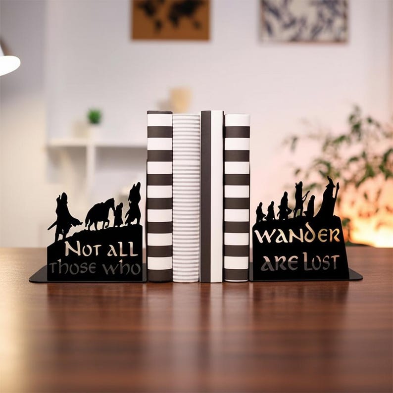 May include: Black metal bookends with silhouette designs. One bookend features a wolf and other animals with the text "Not all those who". The other bookend has a group of people with the text "Wander are Lost". Books are between the bookends.