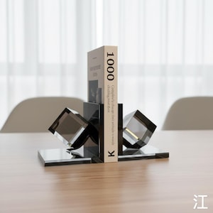 May include: Contemporary bookends in a clear, smoky grey colour. The design features a rectangular base with a cube shape, supporting a book with the number "1000" on the spine. The book's text reads "Completely change their attitude towards clothing treat their".