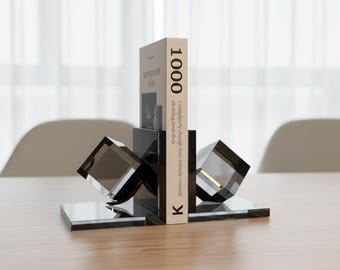 Könnte beinhalten: Moderne, geometrische Buchstützen in transparentem, rauchigem Grau. Die Buchstützen haben eine rechteckige Basis mit einem Würfeldesign und halten ein Buch mit der Nummer "1000" auf dem Buchrücken. Der Text auf dem Buch lautet "Completely change their attitude towards clothing treat their".