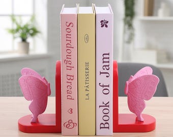 Könnte beinhalten: Rote Buchstützen mit rosa Schmetterlingsakzenten halten drei Bücher. Die Bücher tragen die Titel "Sourdough Bread", "La Pâtisserie" und "Book of Jam". Die Buchstützen stehen auf einer Holzoberfläche.