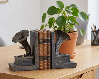 Könnte beinhalten: Ein Paar dunkle, verwitterte Buchstützen in Form von alten Grammophonen mit trichterförmigen Schalltrichtern, die drei Bücher mit den Buchrückenaufschriften Historia und Musica stützen. Die Buchstützen haben eine texturierte Oberfläche.