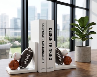 Könnte beinhalten: Weiße Buchstützen mit Football- und Baseball-Design, die zwei Bücher mit den Titeln "CORPORATE SUSTAINABILITY" und "DESIGN THINKING" halten. Ein kleiner Basketball und eine Topfpflanze sind ebenfalls zu sehen.