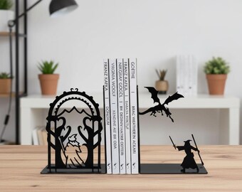 Könnte beinhalten: Schwarze Metall-Buchstützen mit Fantasy-Motiv. Eine Buchstütze zeigt einen Zauberer mit Stab, der einem Drachen gegenübersteht. Die andere hat ein Berg- und Baumdesign. Bücher stehen zwischen den Buchstützen.