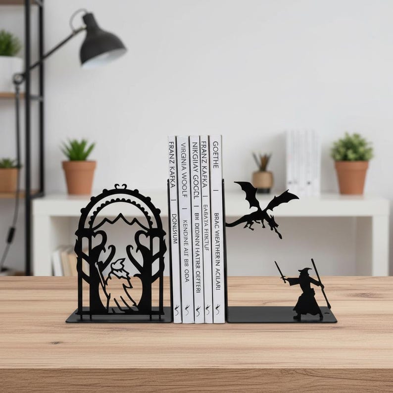 May include: Black metal bookends with a fantasy theme. One bookend features a wizard with a staff, facing a dragon. The other bookend has a mountain and tree design. Books are between the bookends.