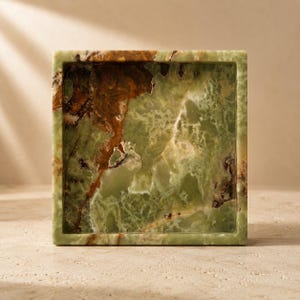 May include: A square tray crafted from green onyx stone, featuring a polished finish and a natural marbled pattern with deep brown and cream-colored veins running throughout the surface, creating a unique and organic appearance for the piece.
