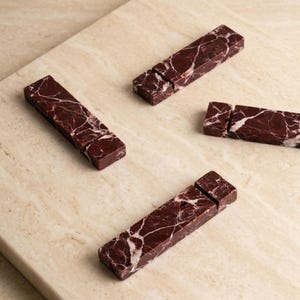 May include: Four rectangular marble pieces with a deep red hue and white veining are arranged on a light beige surface. Each piece is split into two sections, creating a unique design element. The marble's natural patterns add visual interest.