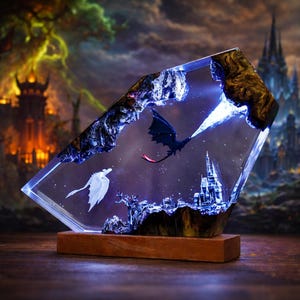 Puede incluir: Escultura de resina de temática fantástica que representa un dragón negro lanzando fuego azul a un dragón blanco. La obra de arte está dentro de un bloque de resina transparente y en ángulo, con un castillo y un fondo estrellado. La base es de madera.